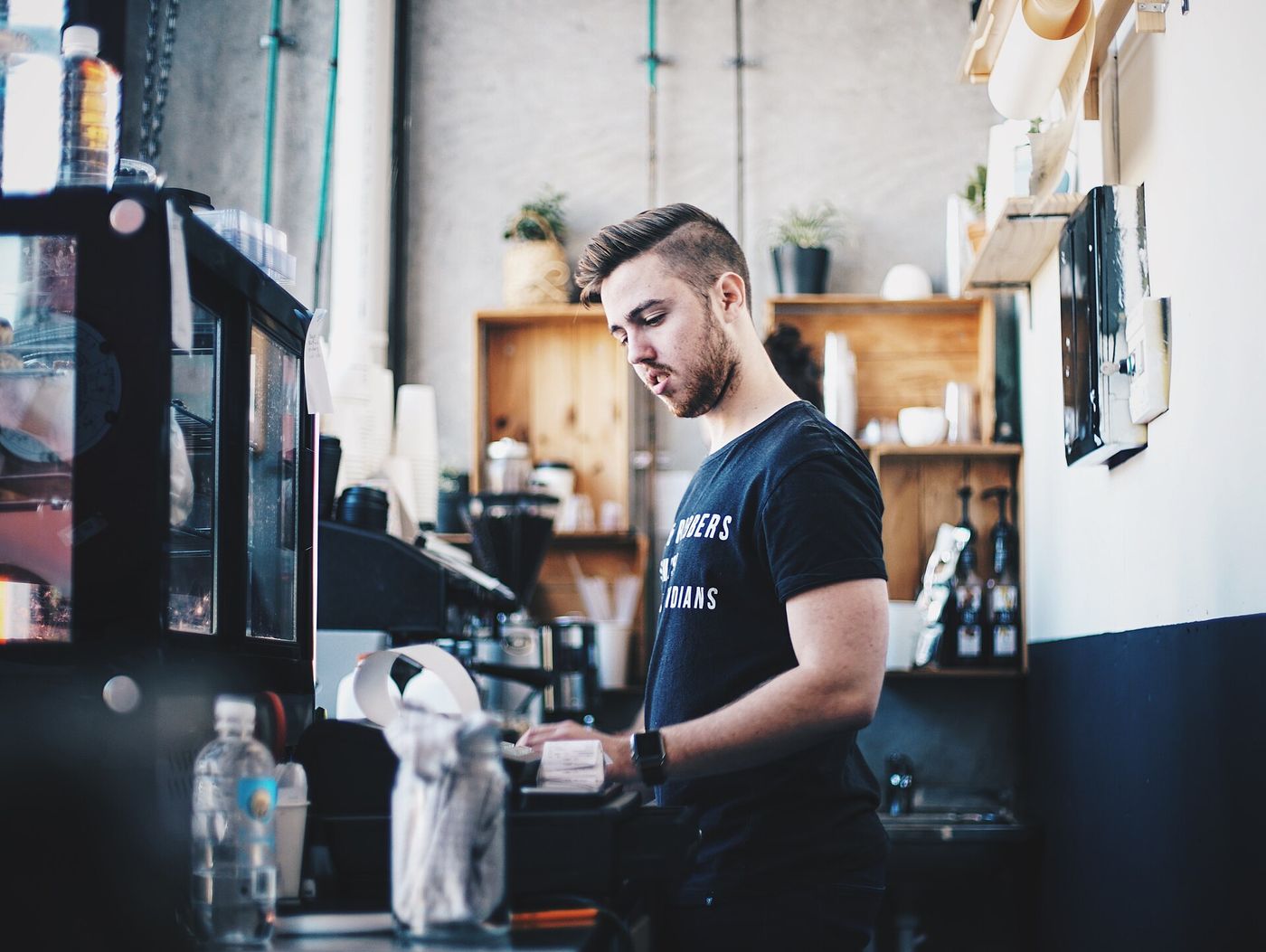 A young man in a black T-shirt works the till behind a café counter